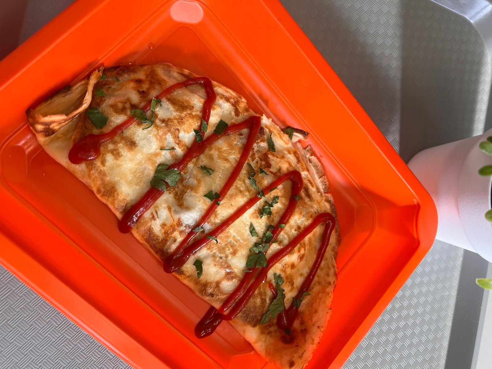 Omlet na pomarańczowym talerzu, polany ketchupem i posypany świeżą kolendrą.