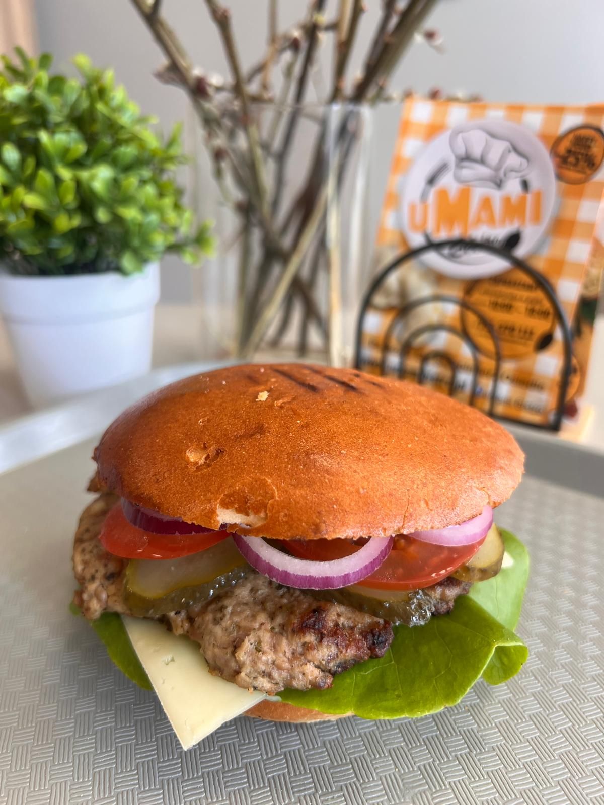 Burgery z soczystym kotletem, serem, sałatą, pomidorami, ogórkiem i cebulą, podane na talerzu z dekoracją.