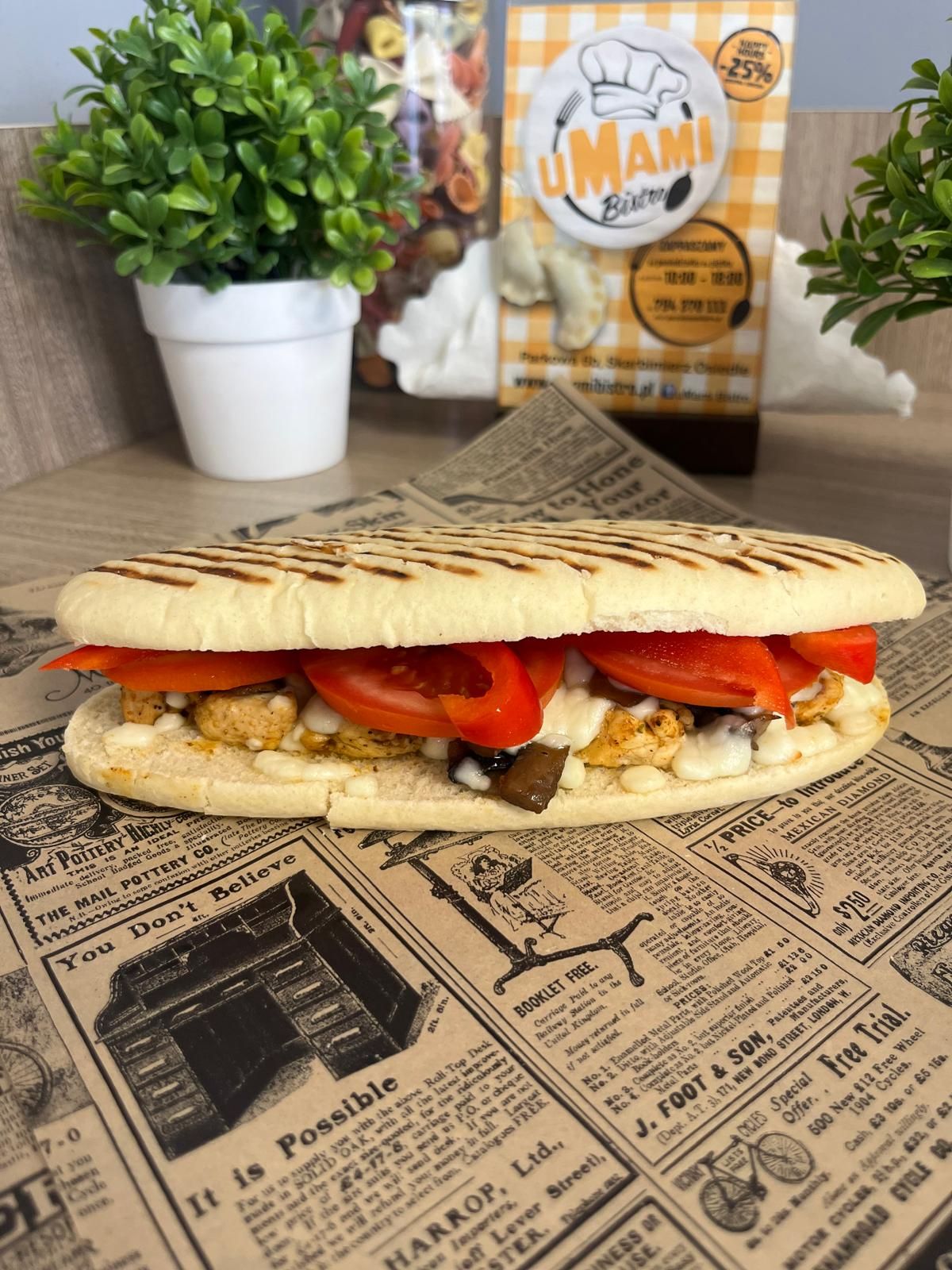Kanapka z grillowanym kurczakiem, pomidorami i kremowym sosem, podana na tle gazetowych wycinków.