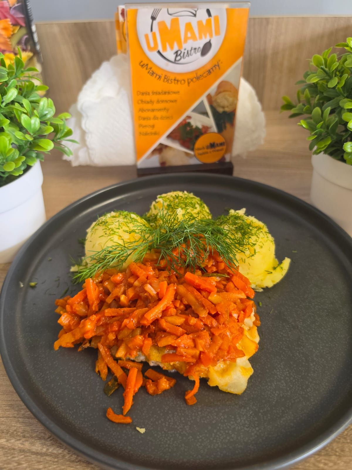 Talerz z ziemniakami, surówką z marchewki i sosem pomidorowym, w tle ulotka Umami Bistro.
