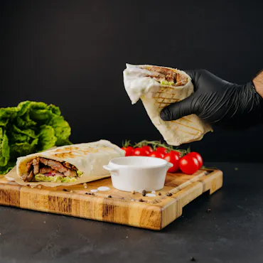 Tortilla z mięsem i warzywami, podana obok sosu, na drewnianej desce, z ciemnym tłem.