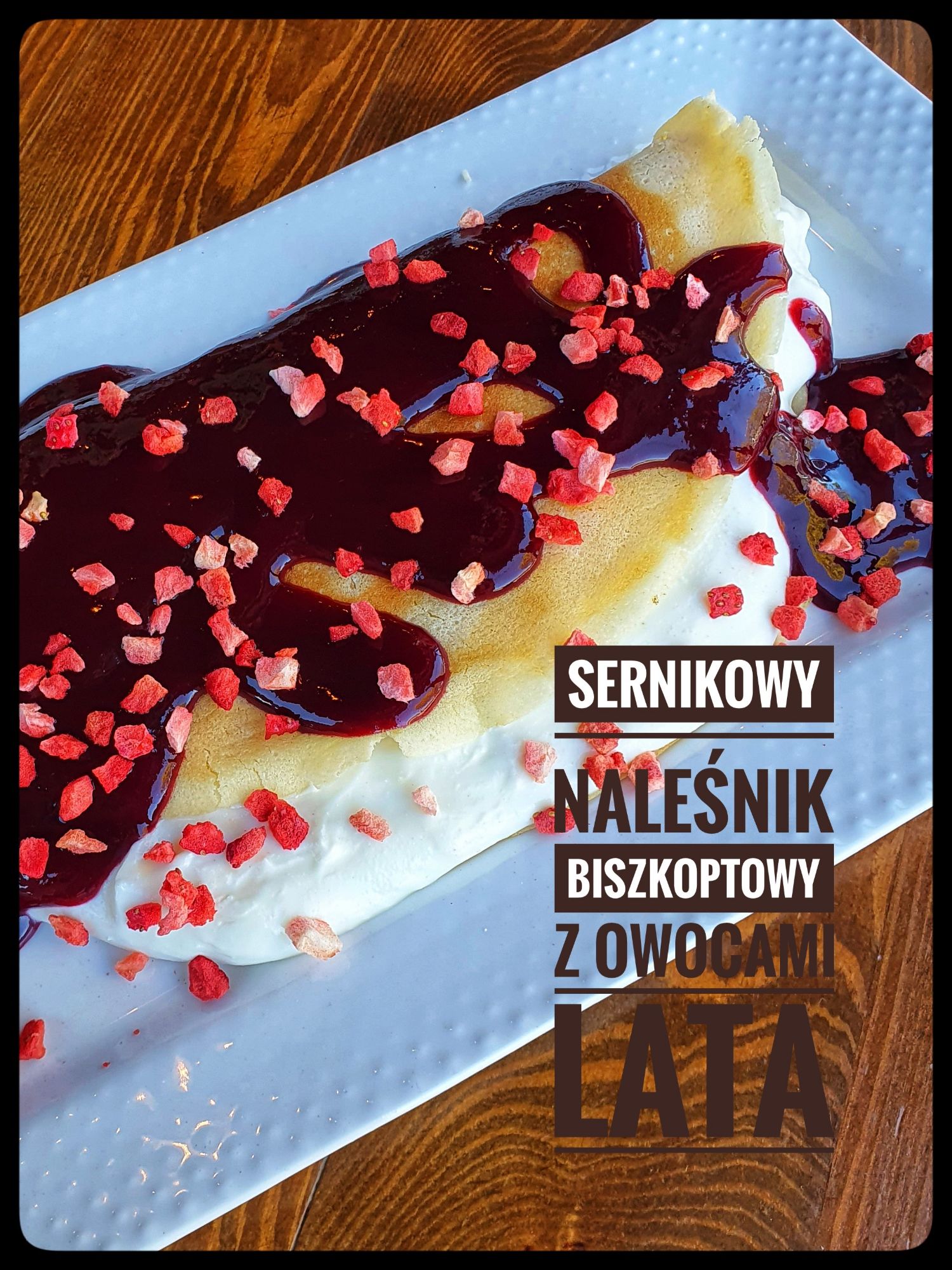 Sernikowy naleśnik biszkoptowy z owocami lata, polewą owocową i posypką truskawkową na białym talerzu.