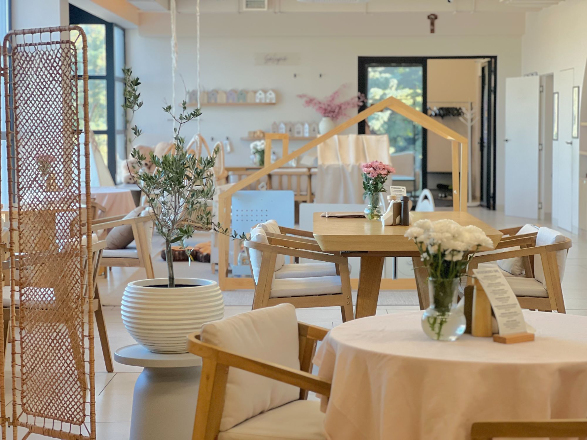 Nowoczesna przestrzeń restauracyjna z drewnianymi meblami, roślinami i jasnymi kolorami.