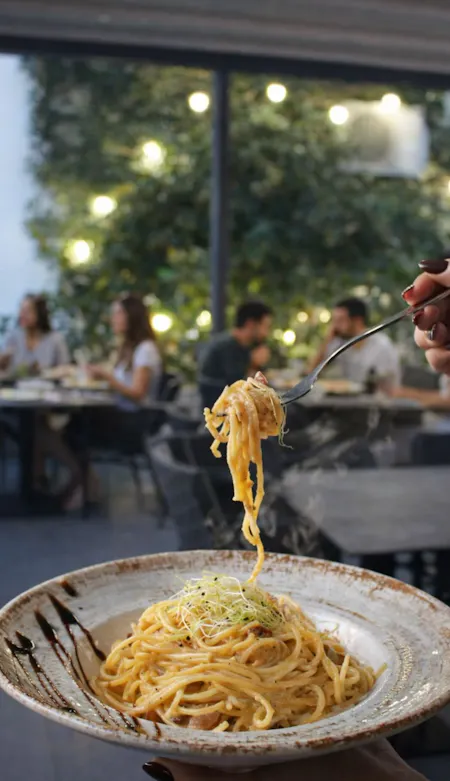 Pasta s umakom, ukrašena zelenilom, u restoranu s gostima i atmosferom.