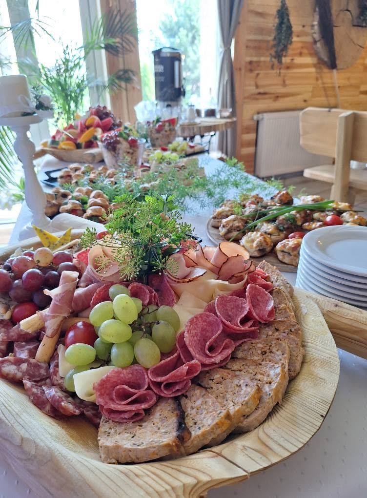 Stół z różnorodnymi przysmakami, w tym wędlinami, serem, owocami i pieczywem w przytulnej scenerii.