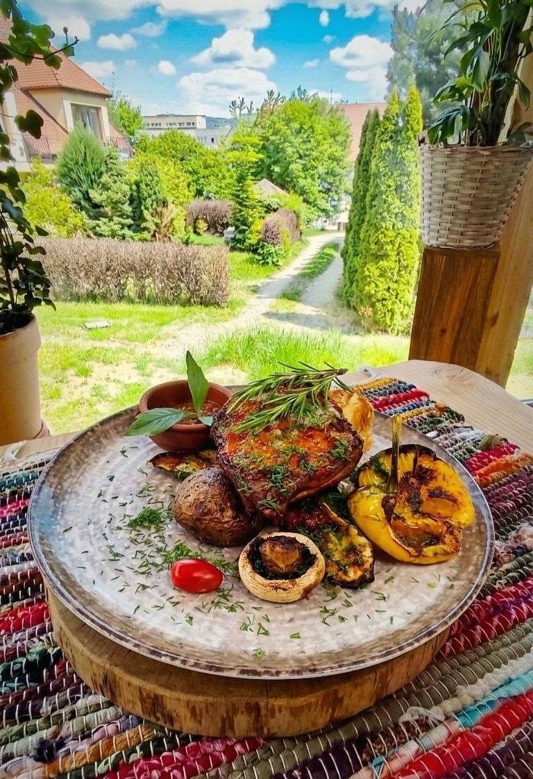 Danie na talerzu z grillowanym mięsem, warzywami i ziołami w tle z widokiem na zielony ogród.