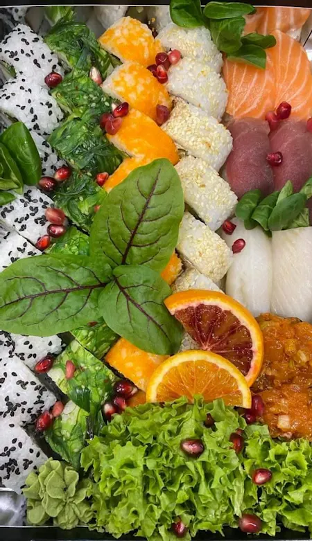 Bento z różnorodnymi sushi, z łososiem, tuńczykiem, warzywami i owocami, podane na liściach sałaty.