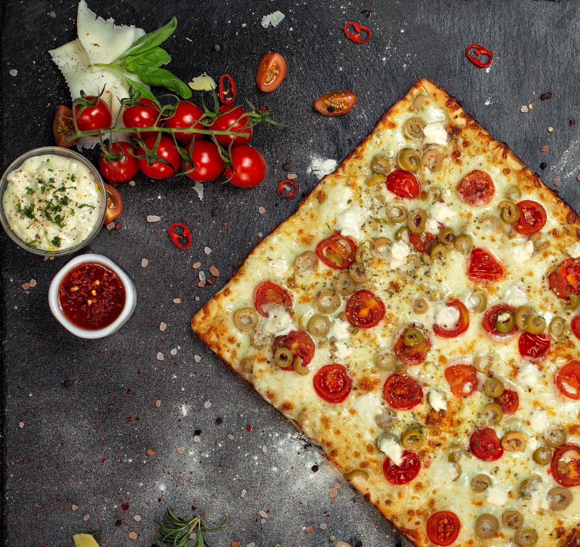 Pizza cu roșii cherry și măsline verzi, garnisită cu brânză, servită pe un fundal de piatră.