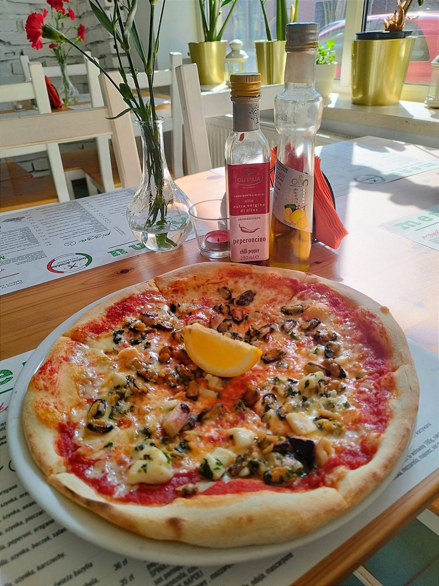 Pizza z owocami morza z cytryną, na stole obok oliwy i wina w restauracji.