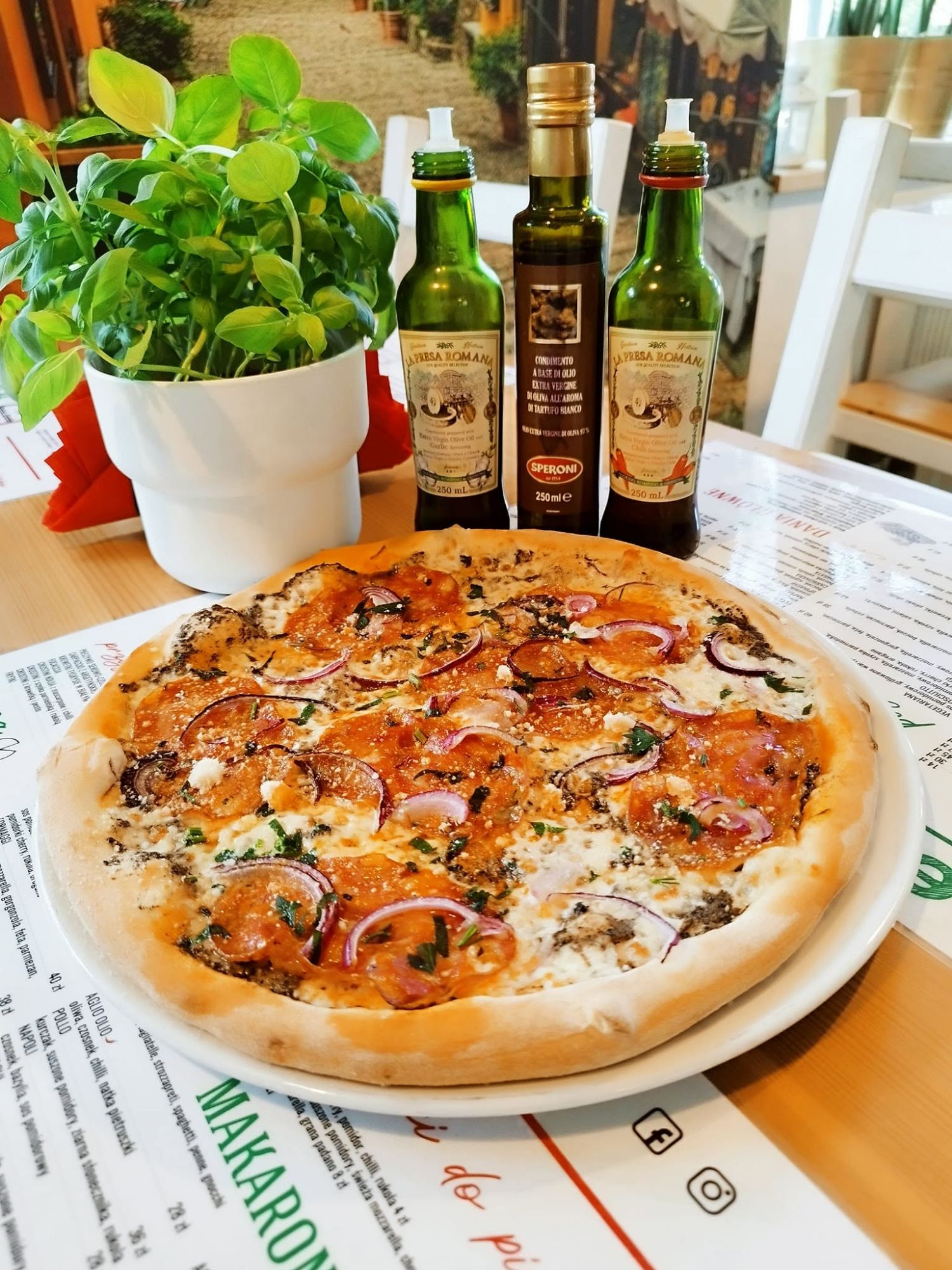 Pizza z wędzonym łososiem, cebulą i sosem, obok butelki oliwy i zioła w doniczce.