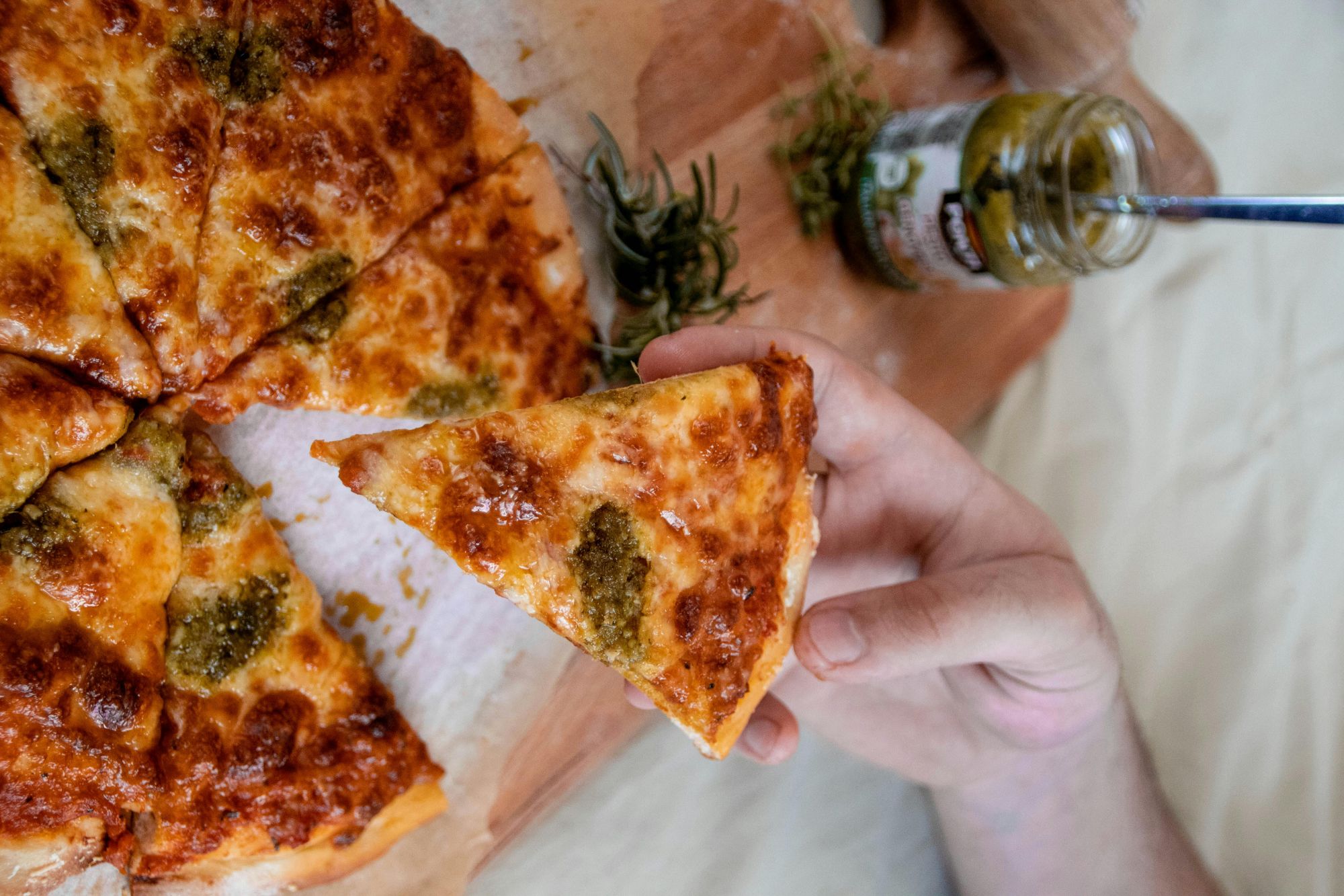 Pizza z serem i ziołowym pesto, kawałek trzymany w dłoni, na drewnianej desce.
