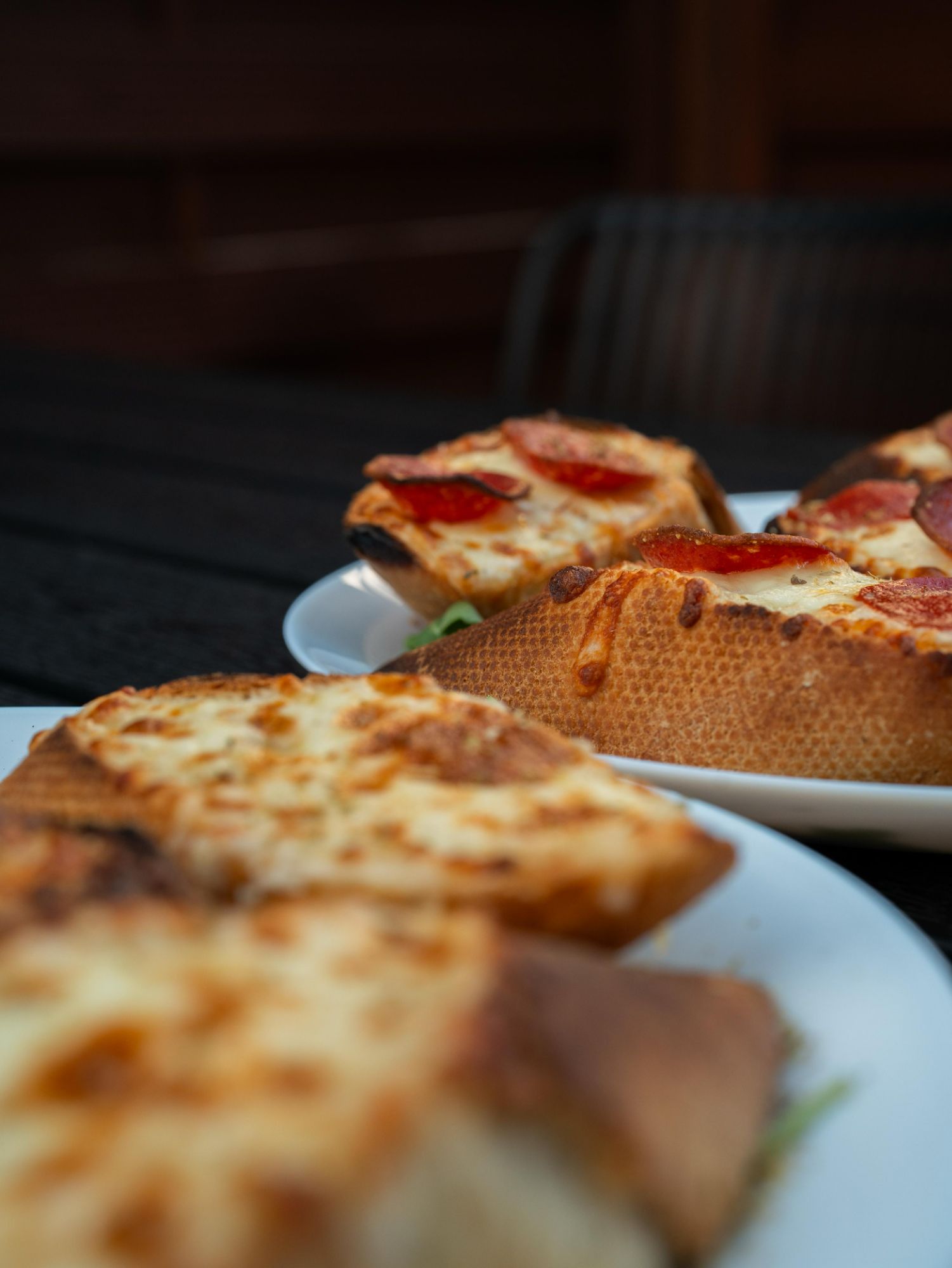 Plasterki pizzy z pepperoni i serem, podane na białym talerzu, z kromkami chleba w tle.
