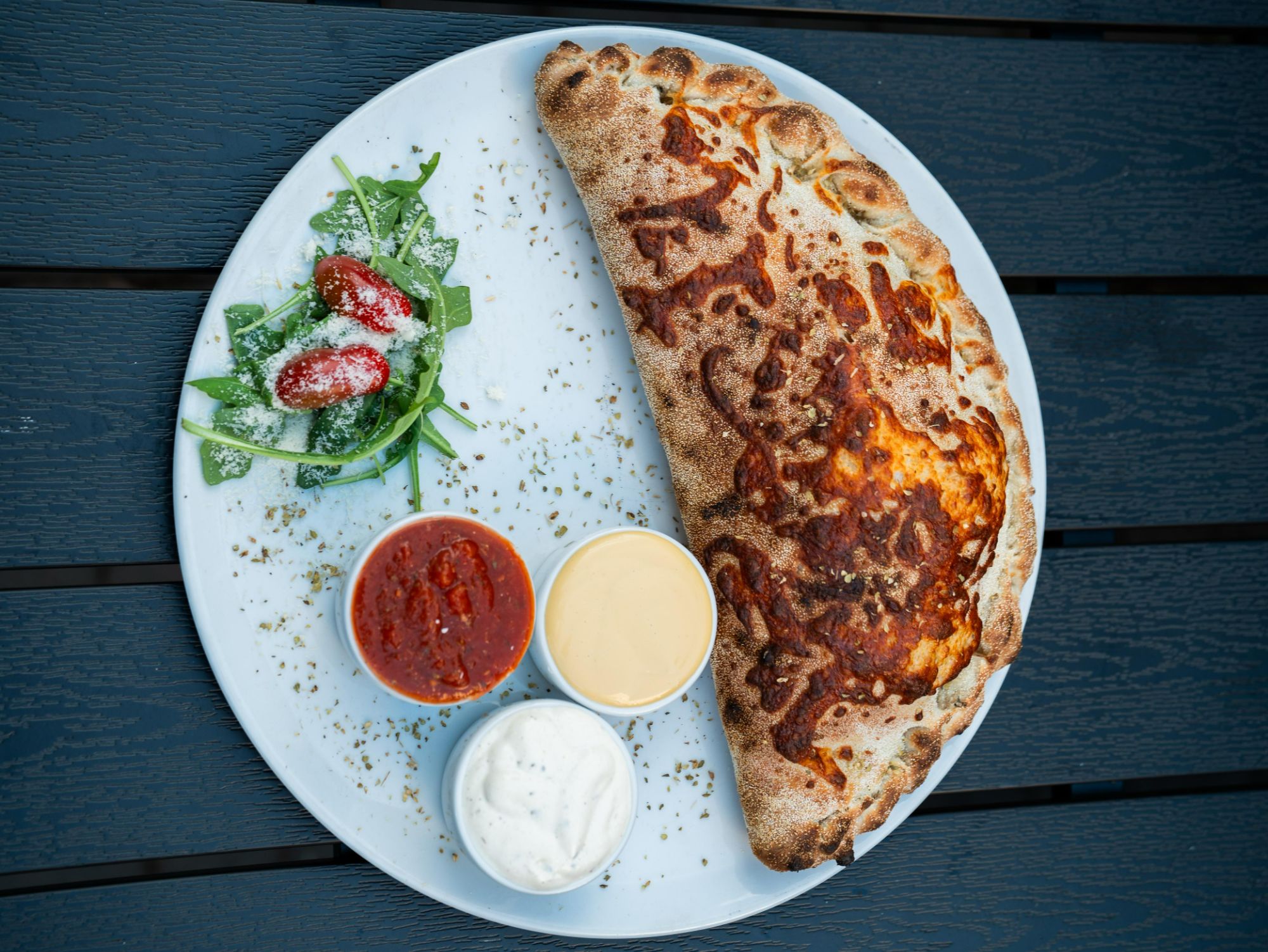 Duża calzone z serem, sosem pomidorowym, białym sosem i sałatą na talerzu.
