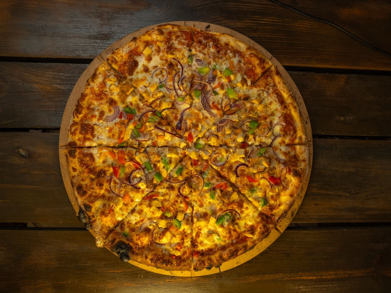 Pizza pokrojona na kawałki, z serem, pepperoni i kolorowymi warzywami, na drewnianym stół.