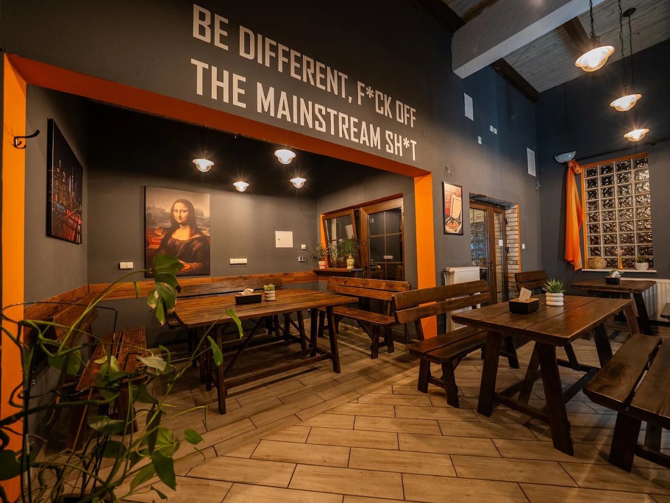 Wnętrze restauracji z drewnianymi stołami, ścianą z napisem i obrazem Mona Lisy.