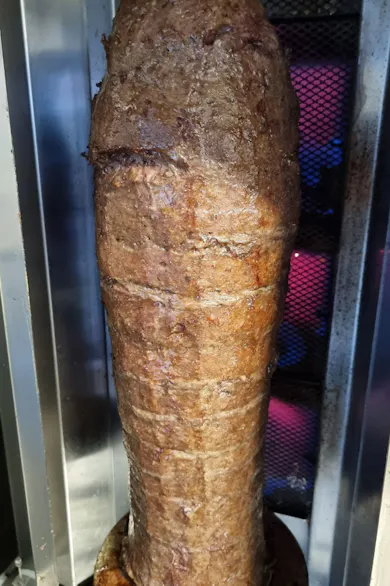 Pojemnik z mięsem do kebaba, obracający się na rożnie, w tle metalowa siatka.
