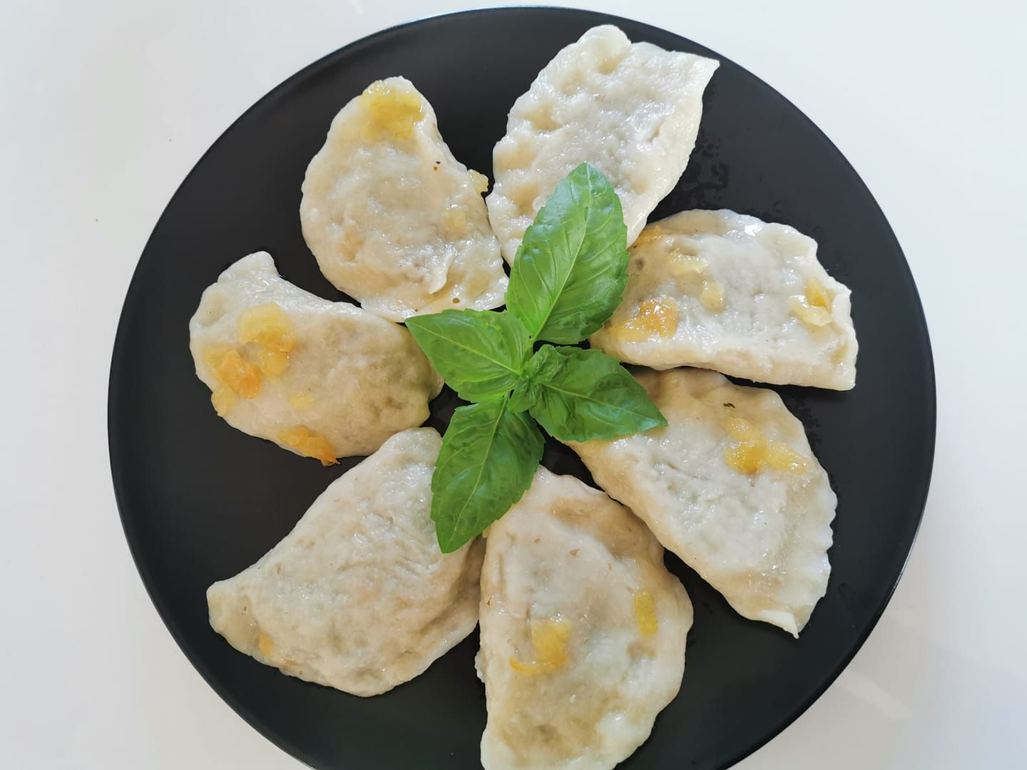 Pierogi na czarnym talerzu, z bazylią na górze, wypełnione farszem z ziemniaków i twarogu.