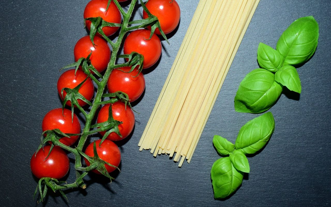 Czerwone pomidory na gałązce, makaron spaghetti i świeża bazylia na czarnym tle.