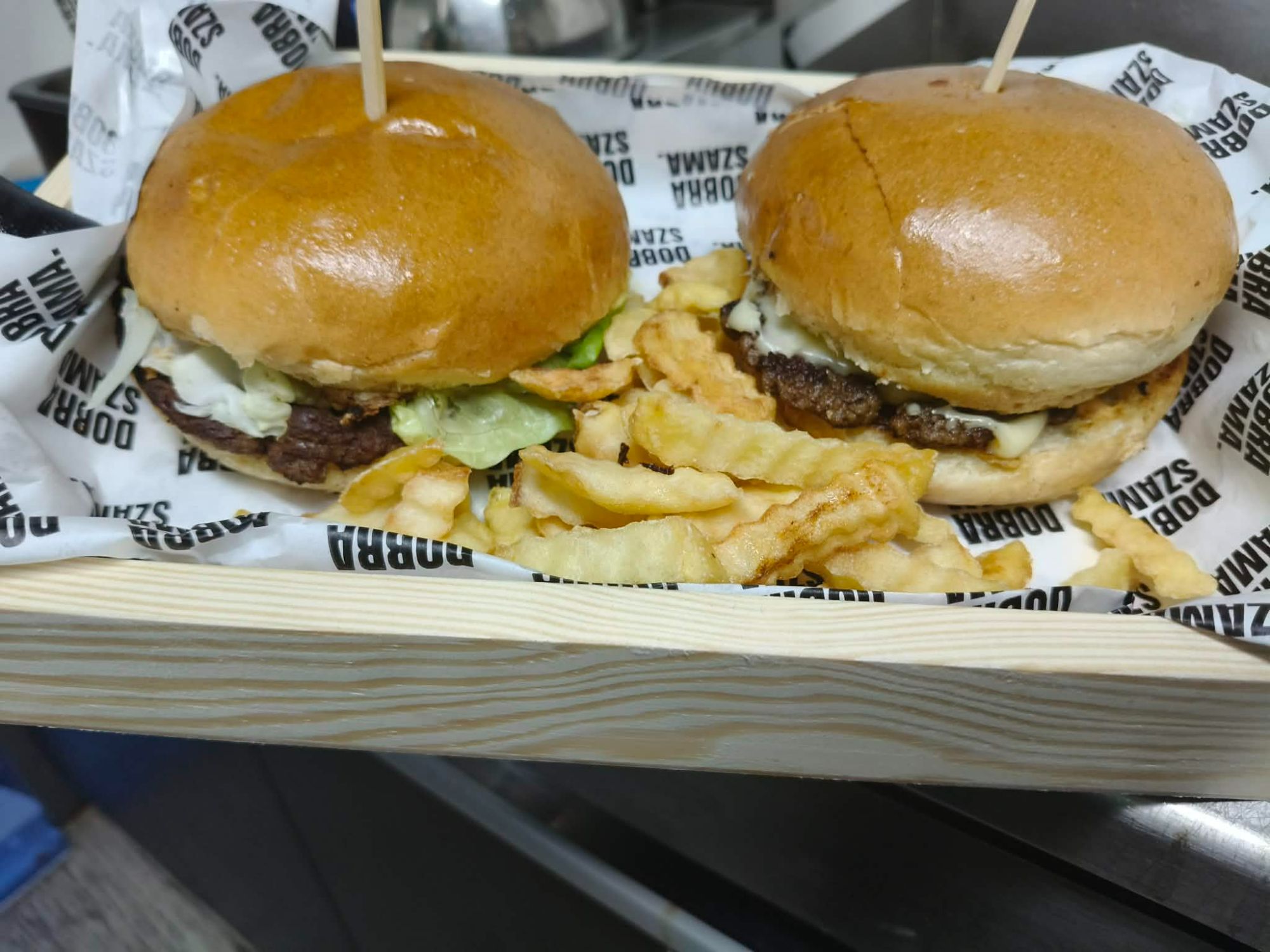 Dwa burgery z mięsem i sałatą, podane z frytkami w drewnianym koszyku.