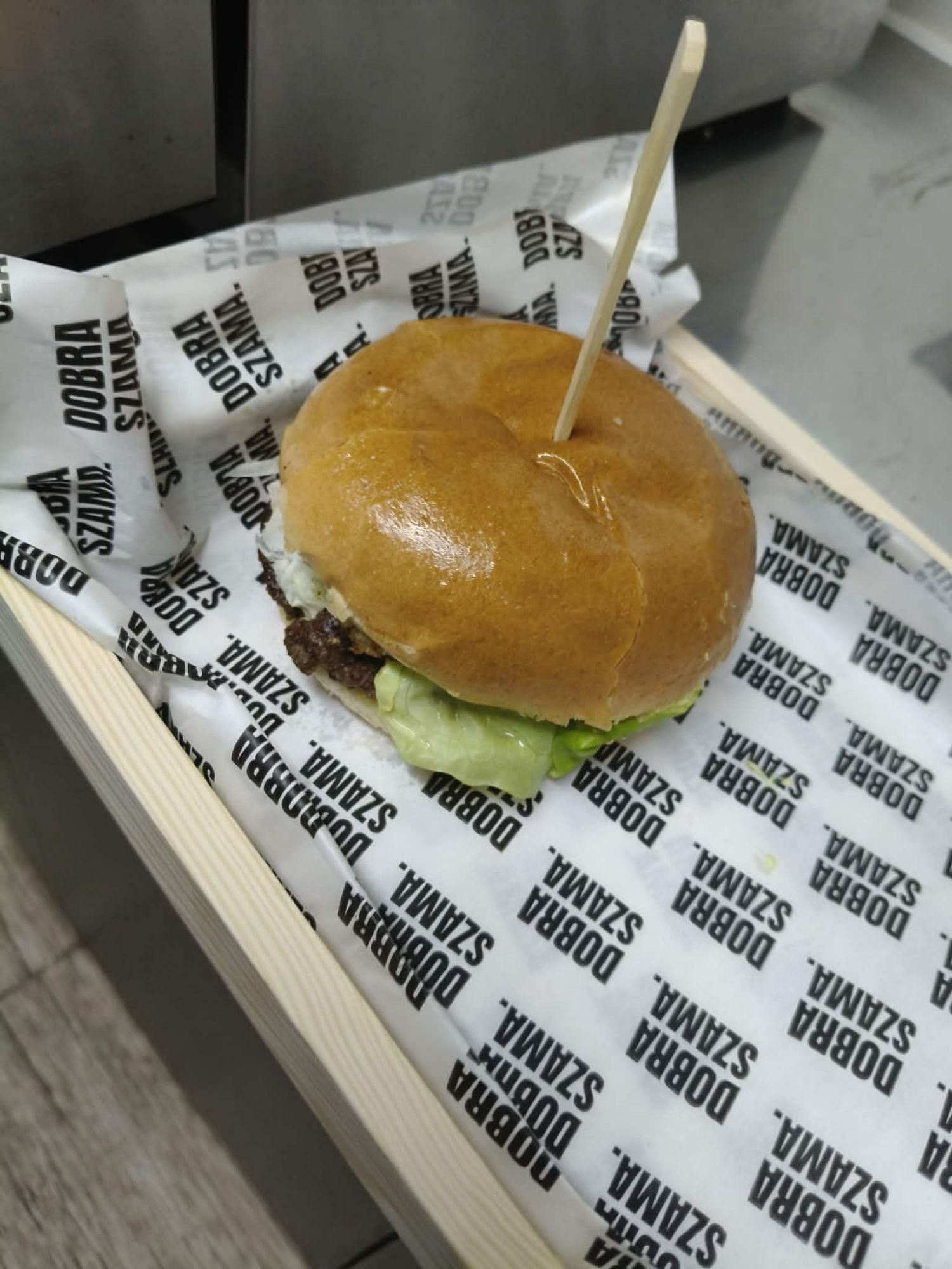 Burger na drewnianym talerzu, podany na papierze z logo restauracji.