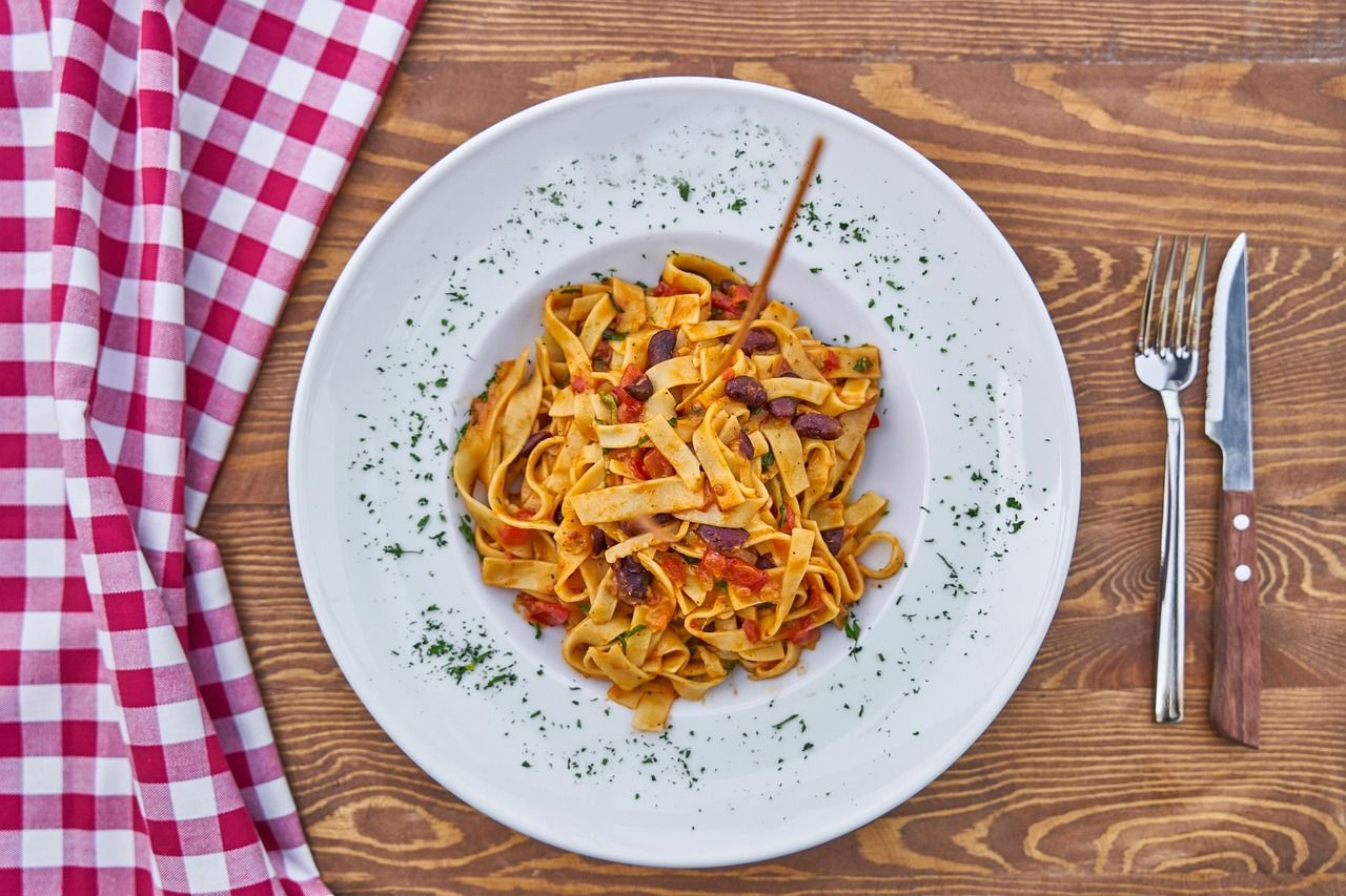 Talerz makaronu fettuccine z sosem pomidorowym, oliwkami i natką pietruszki, na drewnianym stole.
