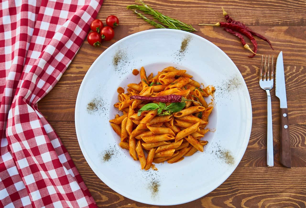 Talerz z makaronem penne w sosie pomidorowym, ozdobiony bazylią i suszonymi chili, podany na drewnianym stole.