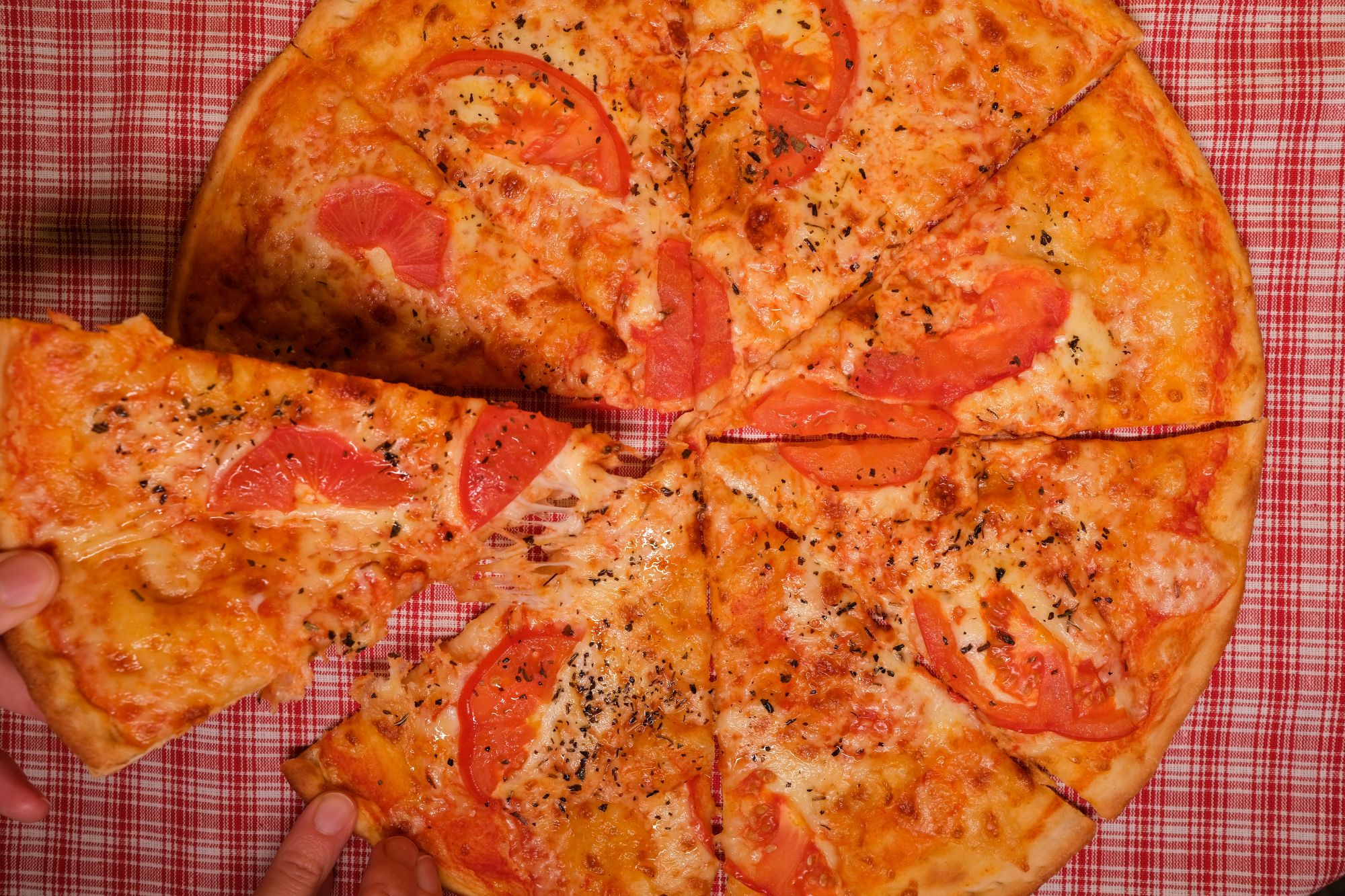 Pizza z serem i plastrami pomidora na kratkowanej tkaninie.