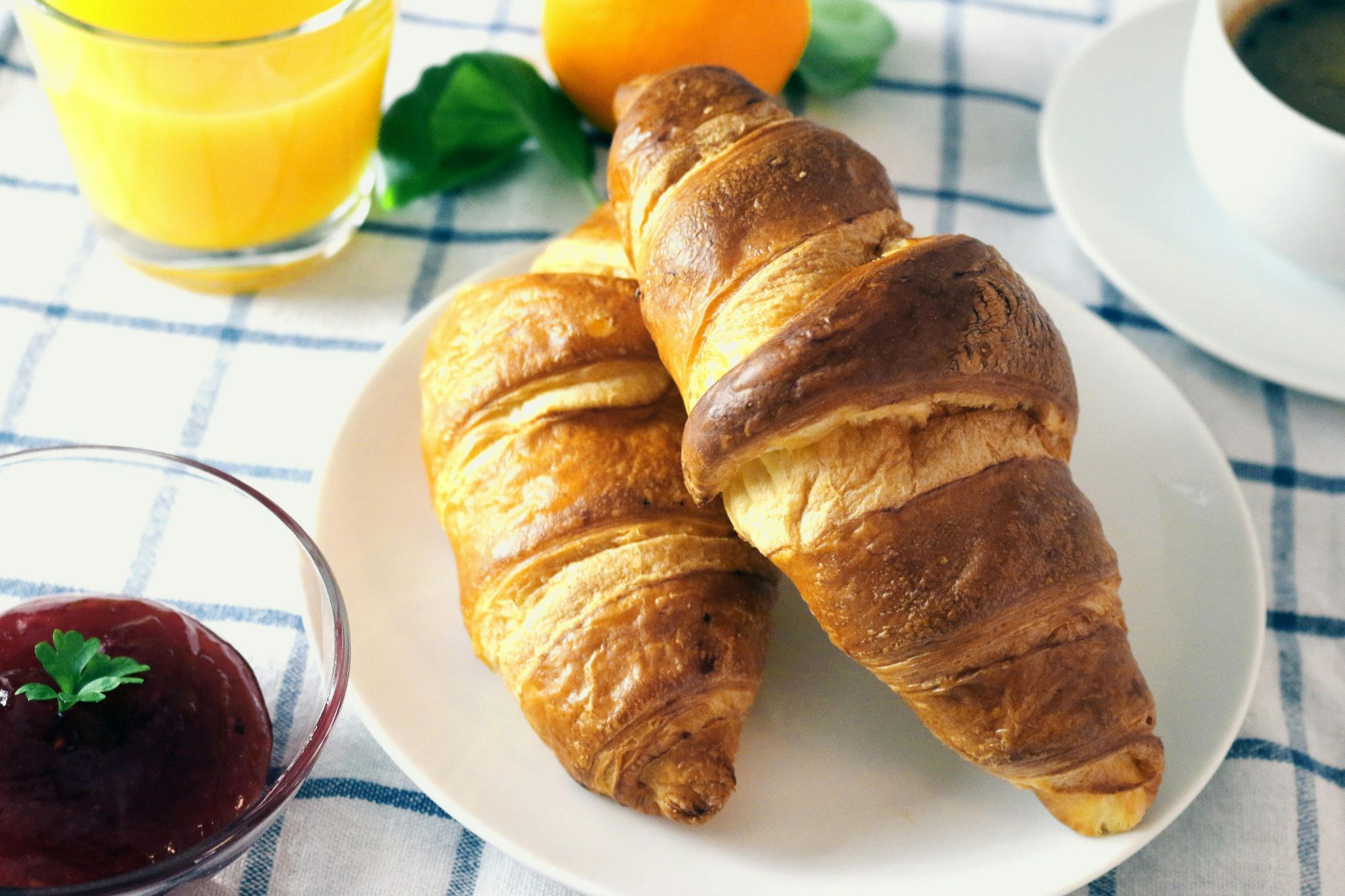 Ciepłe, świeże rogaliki na talerzu obok dżemu, soku pomarańczowego i filiżanki kawy.
