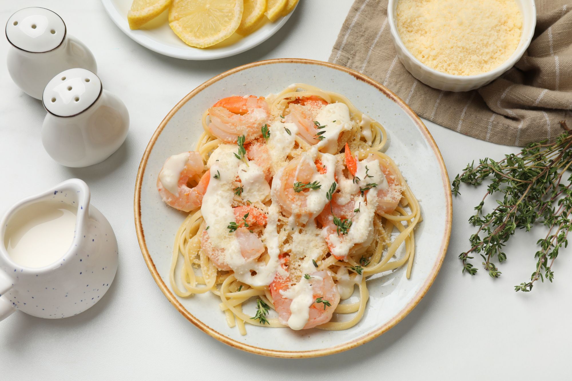 Makaron z krewetkami w sosie śmietanowym, ozdobiony tymiankiem, podany z cytryną i parmezanem.