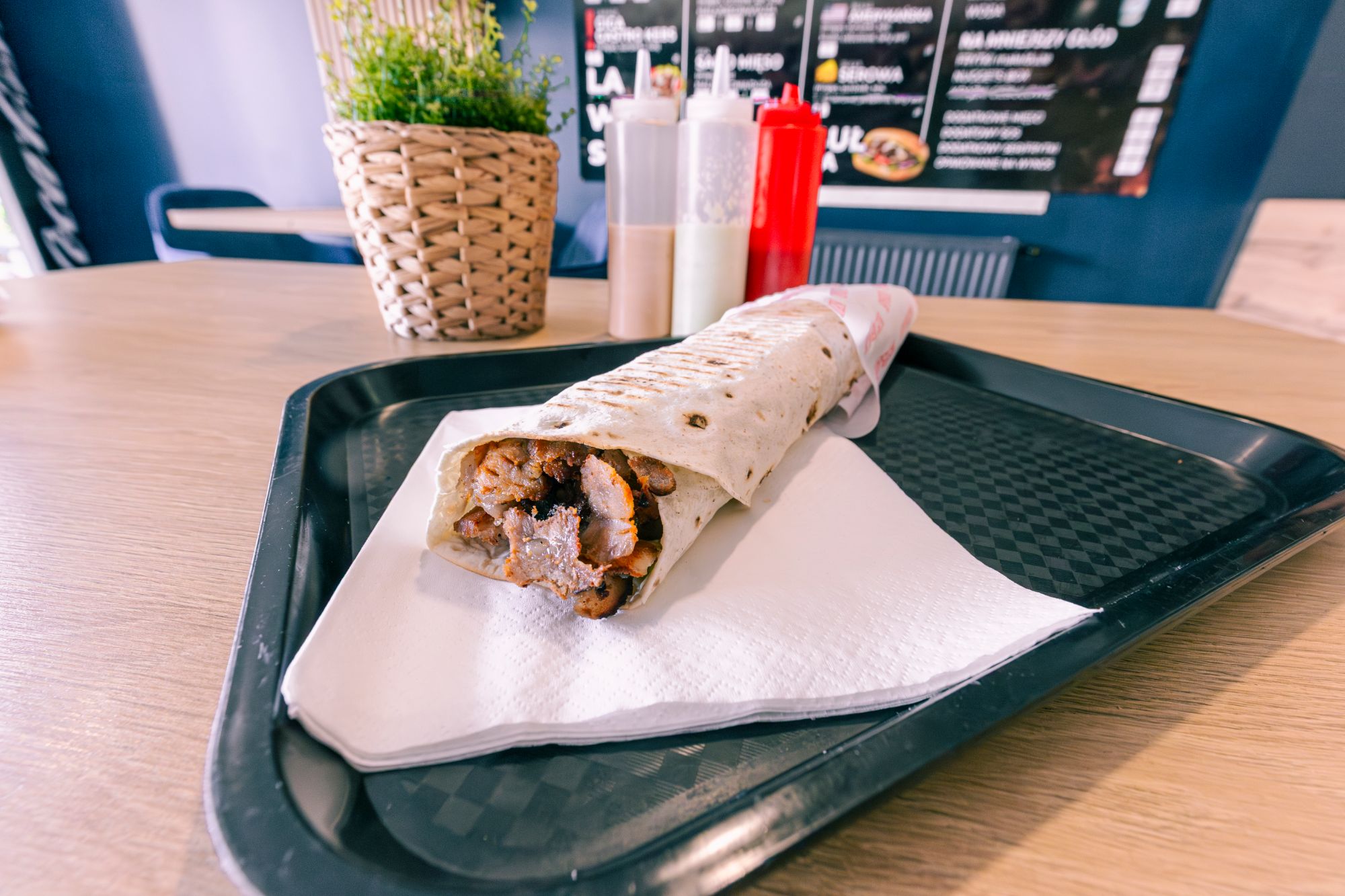 Tortilla z mięsem w barze, podana na czarnym tacy, z sosami w tle i roślinną dekoracją.