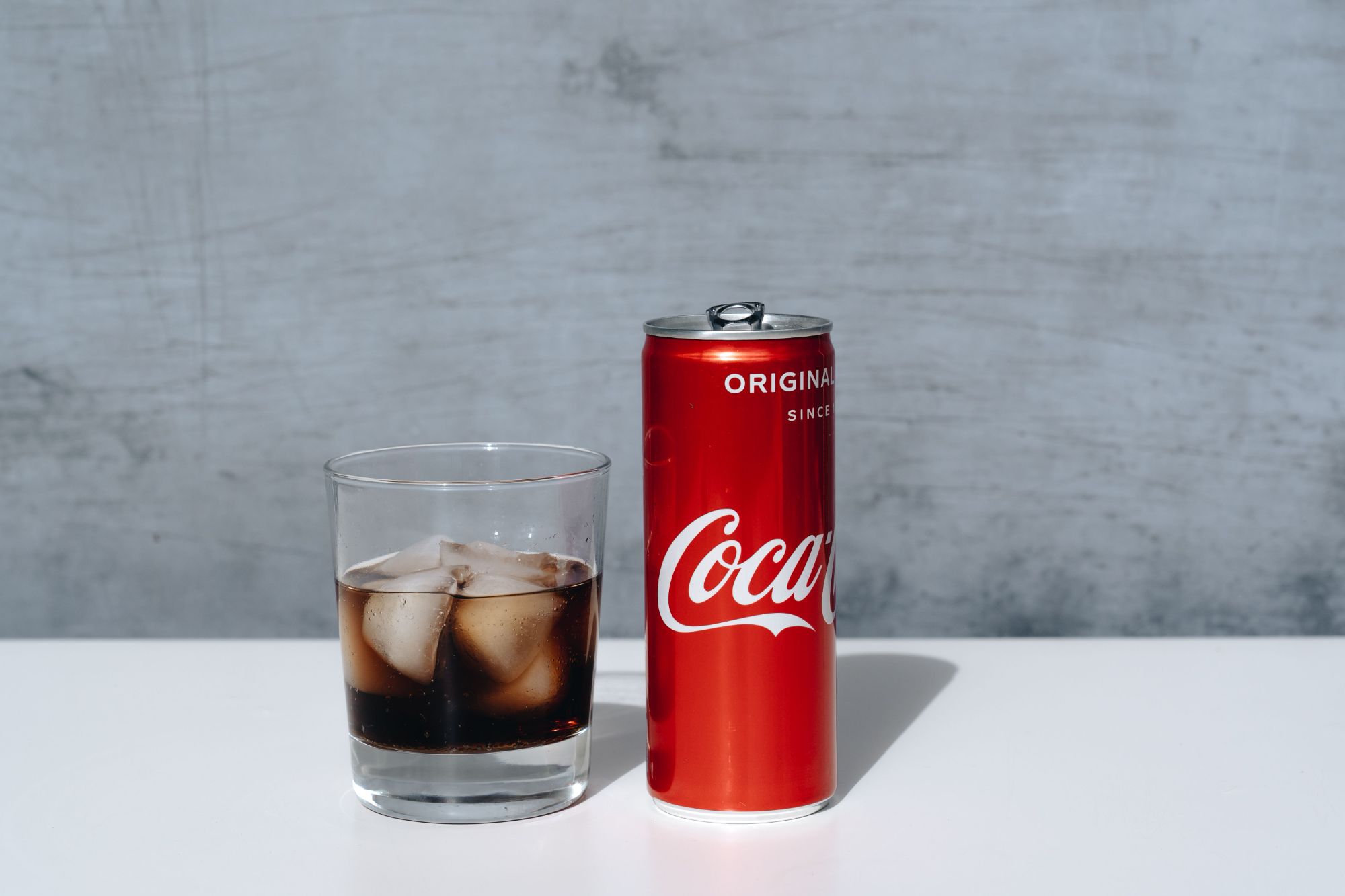 Puszka Coca-Coli obok szklanki z lodem i napojem.