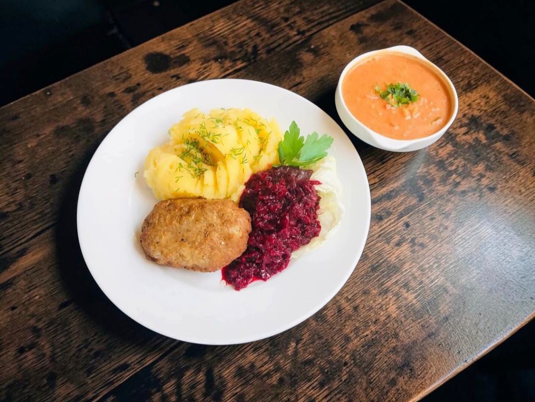 Ziemniaki, kotlet mielony, buraczki i zupa krem w miseczce na drewnianym stole.