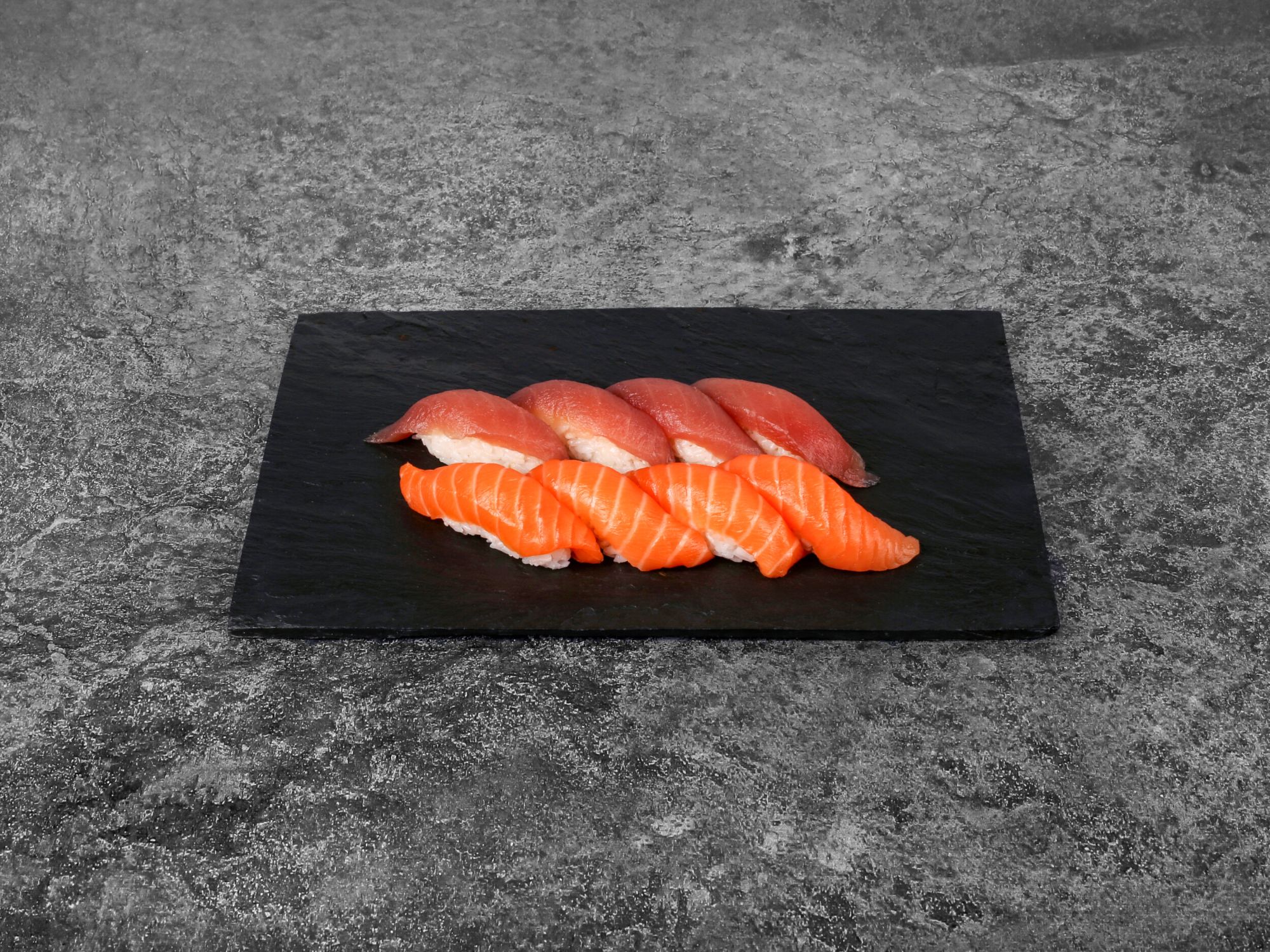 Sushi na czarnej desce, w tym różowy łosoś i inne rodzaje ryb, na szarej powierzchni.