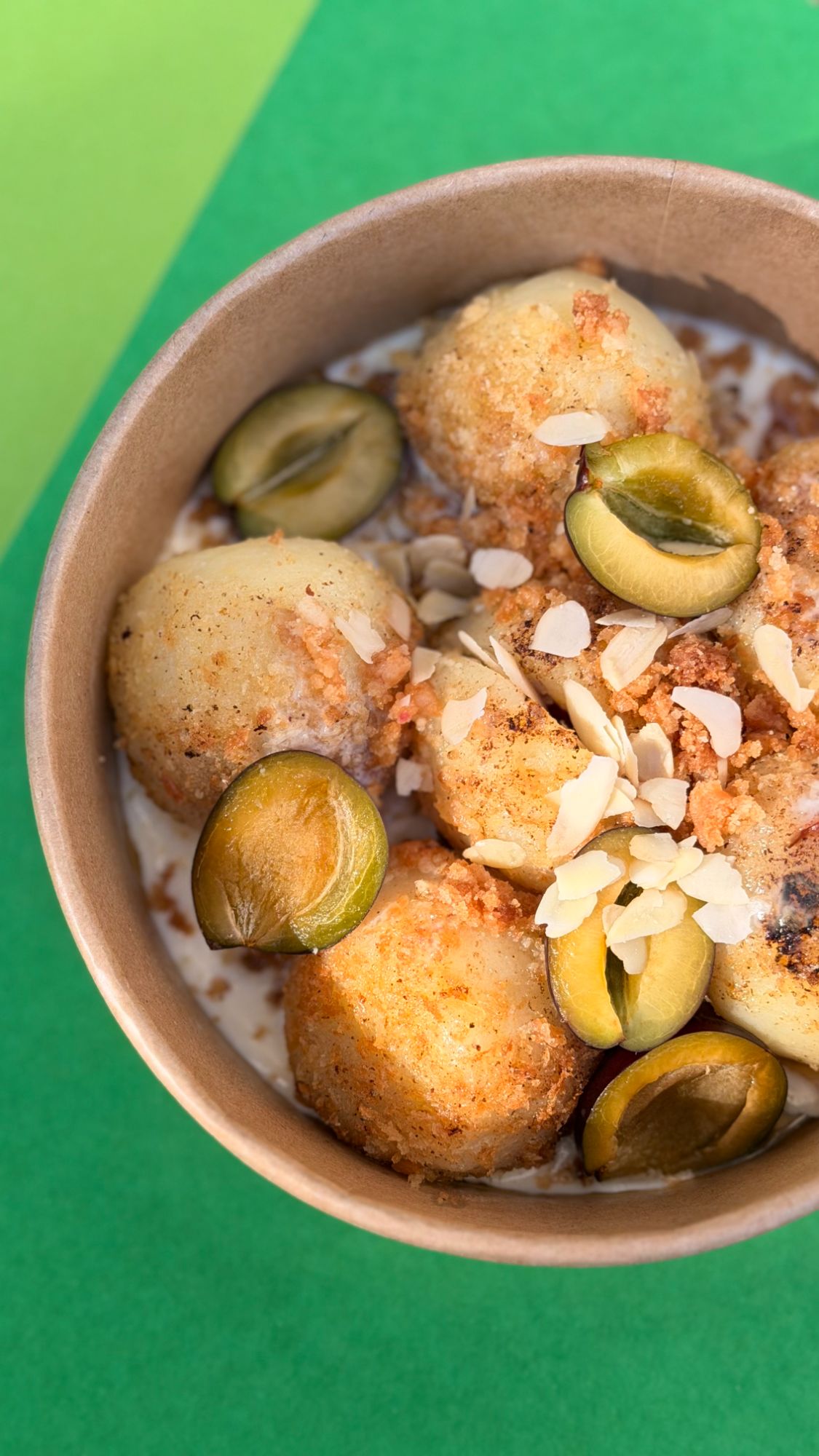 Rice ball in a bowl with pistachios, almond flakes, and crispy crumble against a green background.