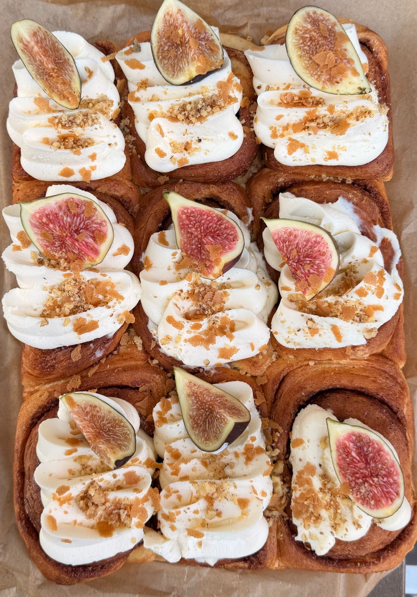 Cinnamon rolls with whipped cream, figs, and crumble on parchment paper.