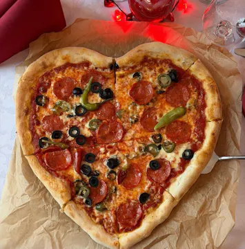 Serca pizza na brązowej pergaminowej dużej desce, z pepperoni, czarnymi oliwkami i zieloną papryką.