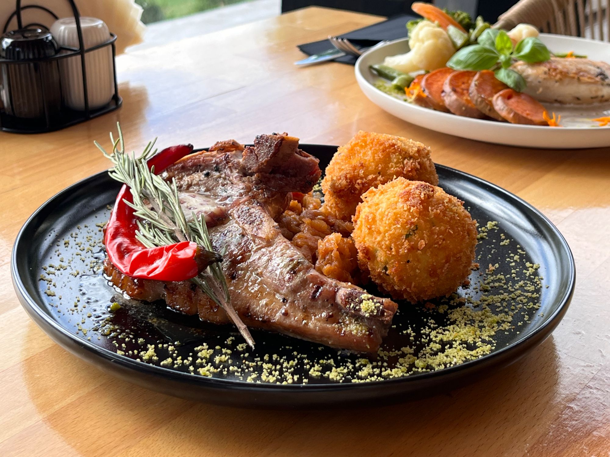 Grillowana kotlet wieprzowy z papryką, ryżowymi kulkami i ziołami na czarnym talerzu.