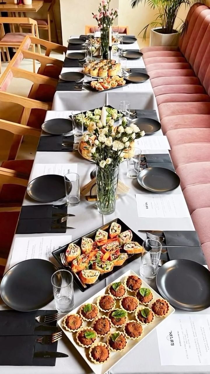 Stół z jedzeniem w restauracji, na którym znajdują się mini tarty, kanapki i bukiet kwiatów.