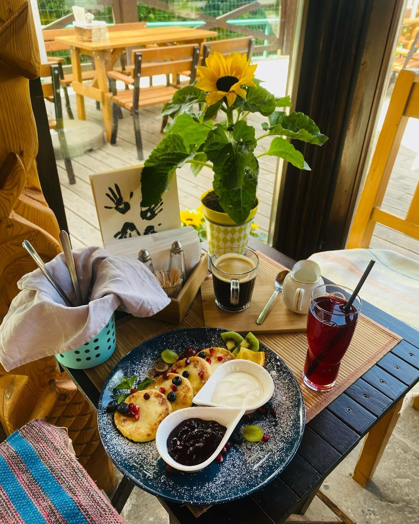 Placemat z pierogami i dodatkami, napój w szklance i kwiat słonecznika na stole w przytulnej kawiarni.