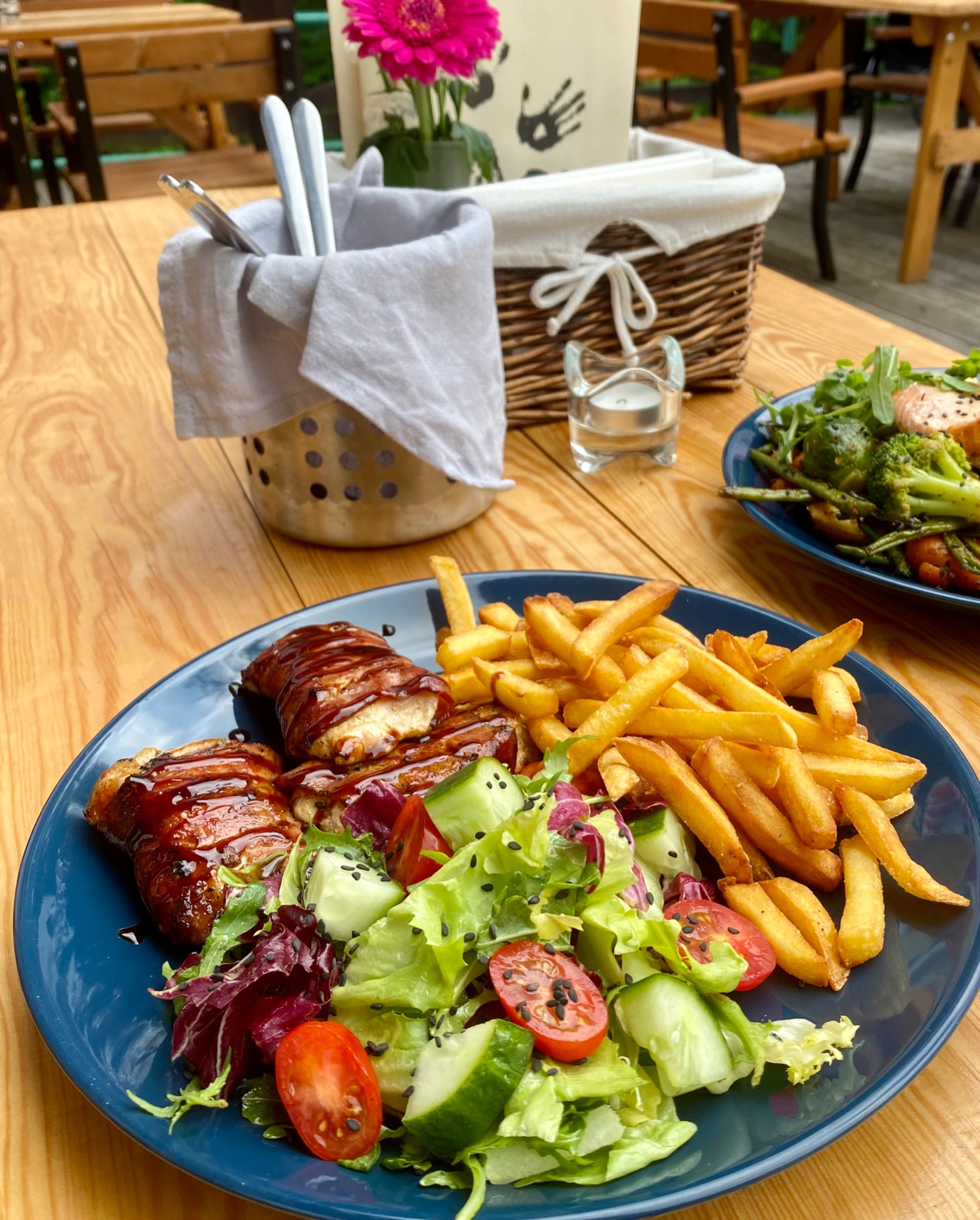 Talerz z kurczakiem w boczku, frytkami i sałatką, podany na drewnianym stole w restauracji.
