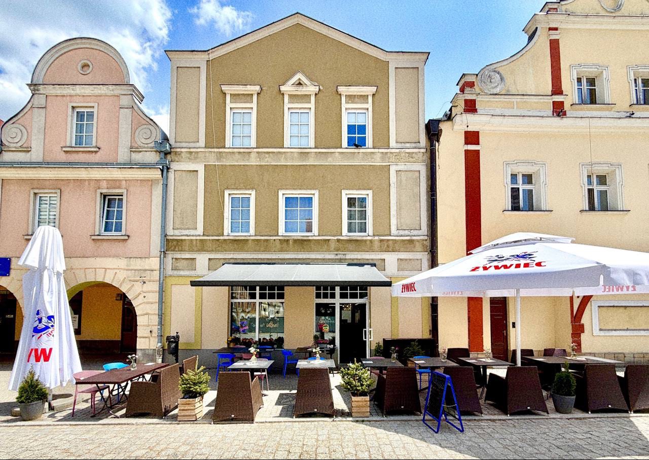 Kawiarnia z parasolami w centrum miasta, otoczona kolorowymi budynkami i jasnym niebem.