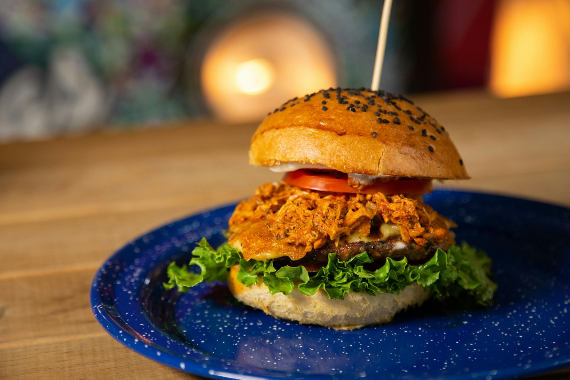 Soczysty burger z kurczakiem, sałatą, pomidorem i bułką z czarnym sezamem na niebieskim talerzu.