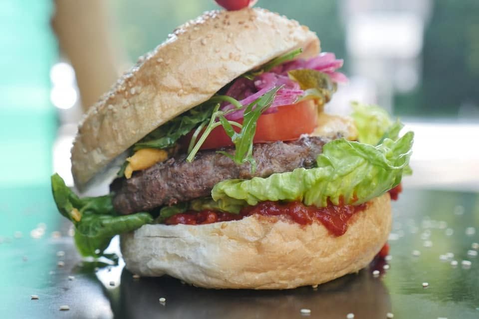 Soczysty burger z wołowiny, sałatą, pomidorem, piklami i sosem na bułce sezamowej.