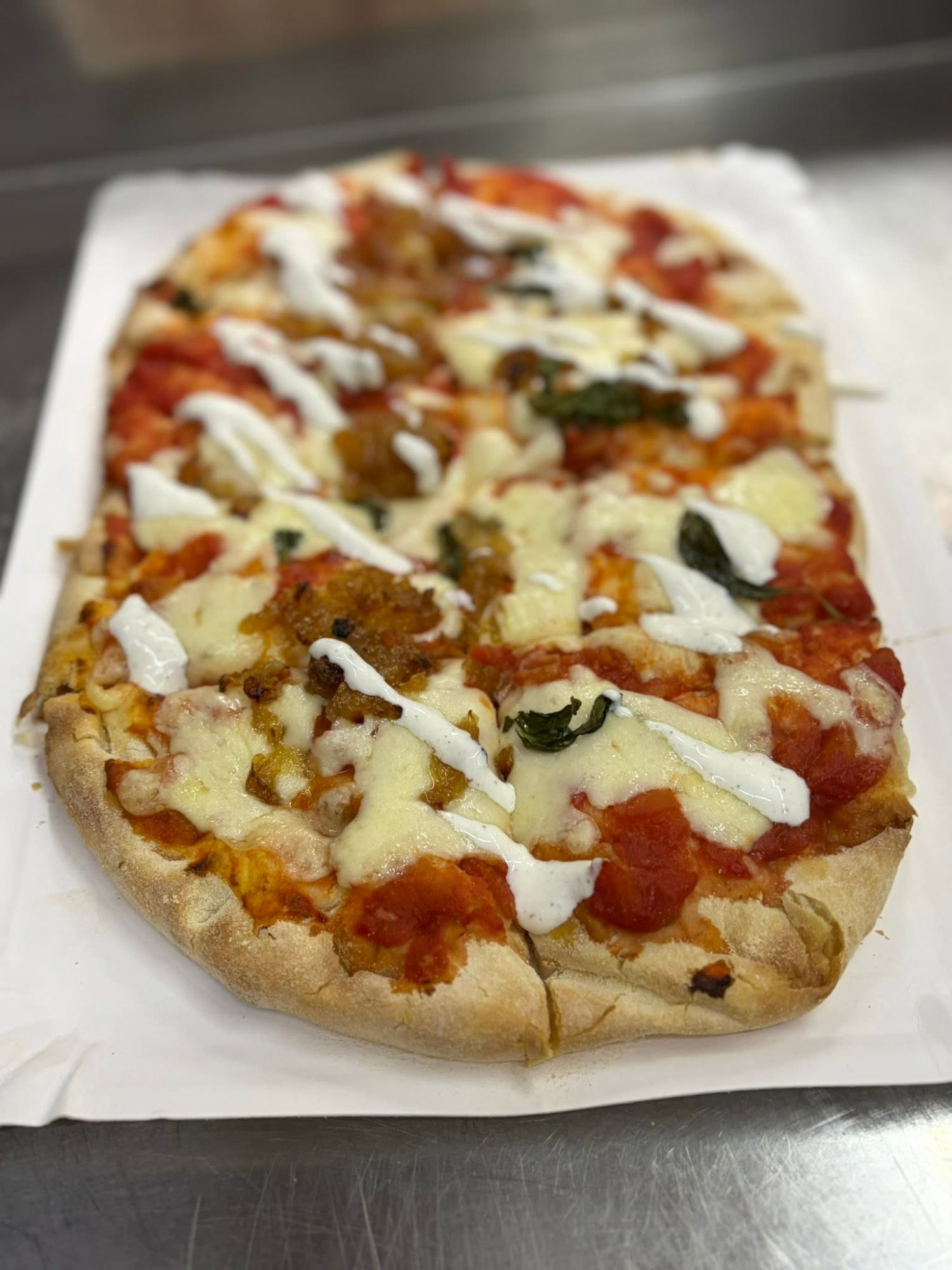 Pizza na cienkim cieście z sosem pomidorowym, serem, mięsem i ziołami, podana na białym papierze.