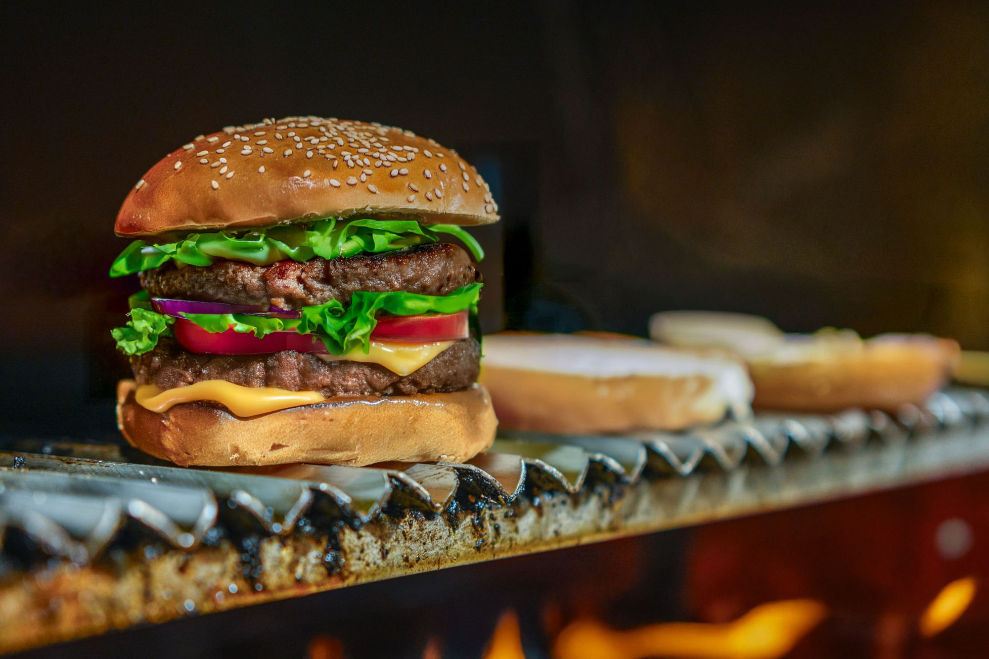 Soczysty burger z warstwami sałaty, pomidora, sera i kotleta wołowego na podpieczonej bułce sezamowej.
