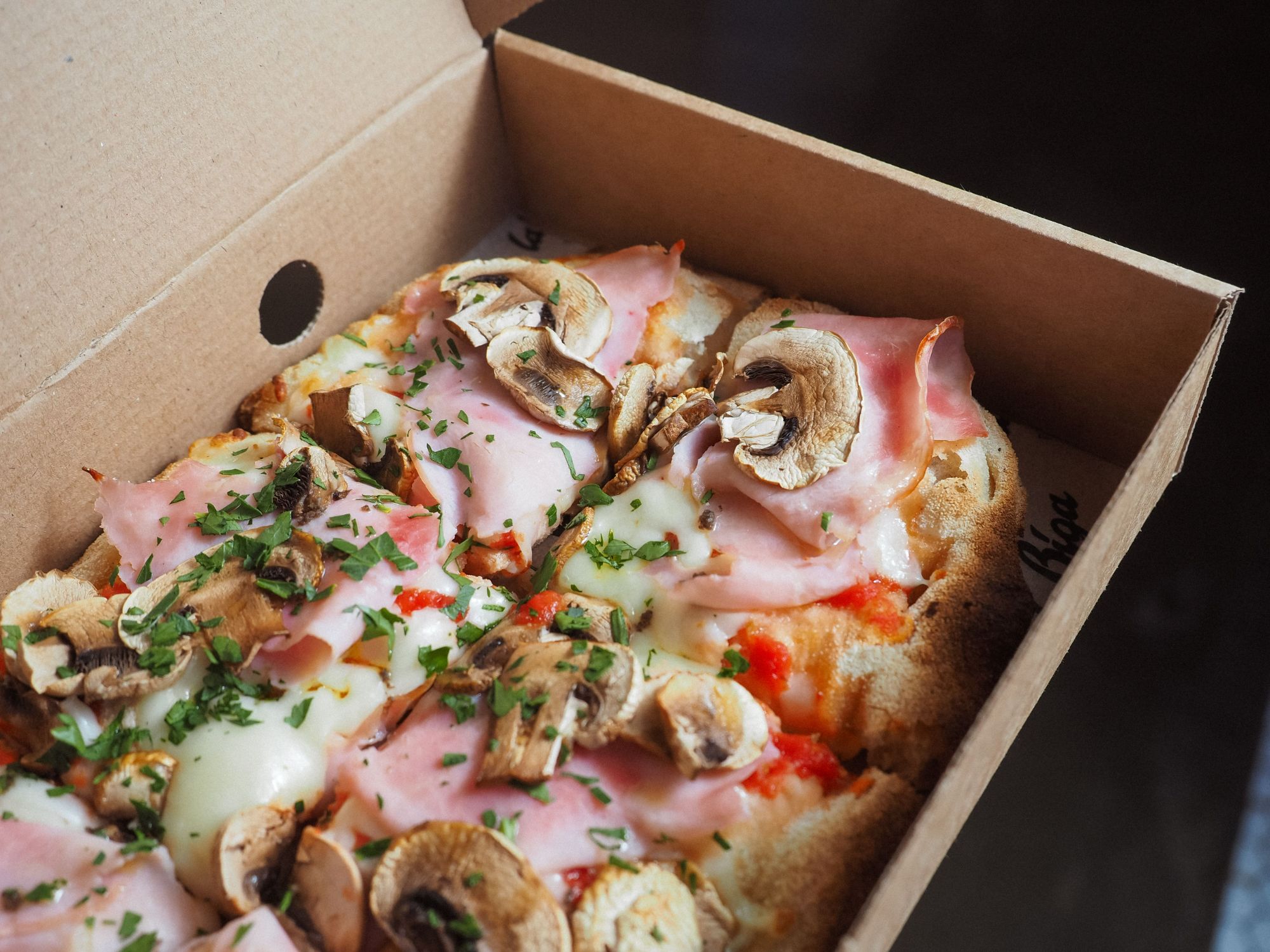 Pizza w pudełku, z szynką, grzybami, serem i ziołami.
