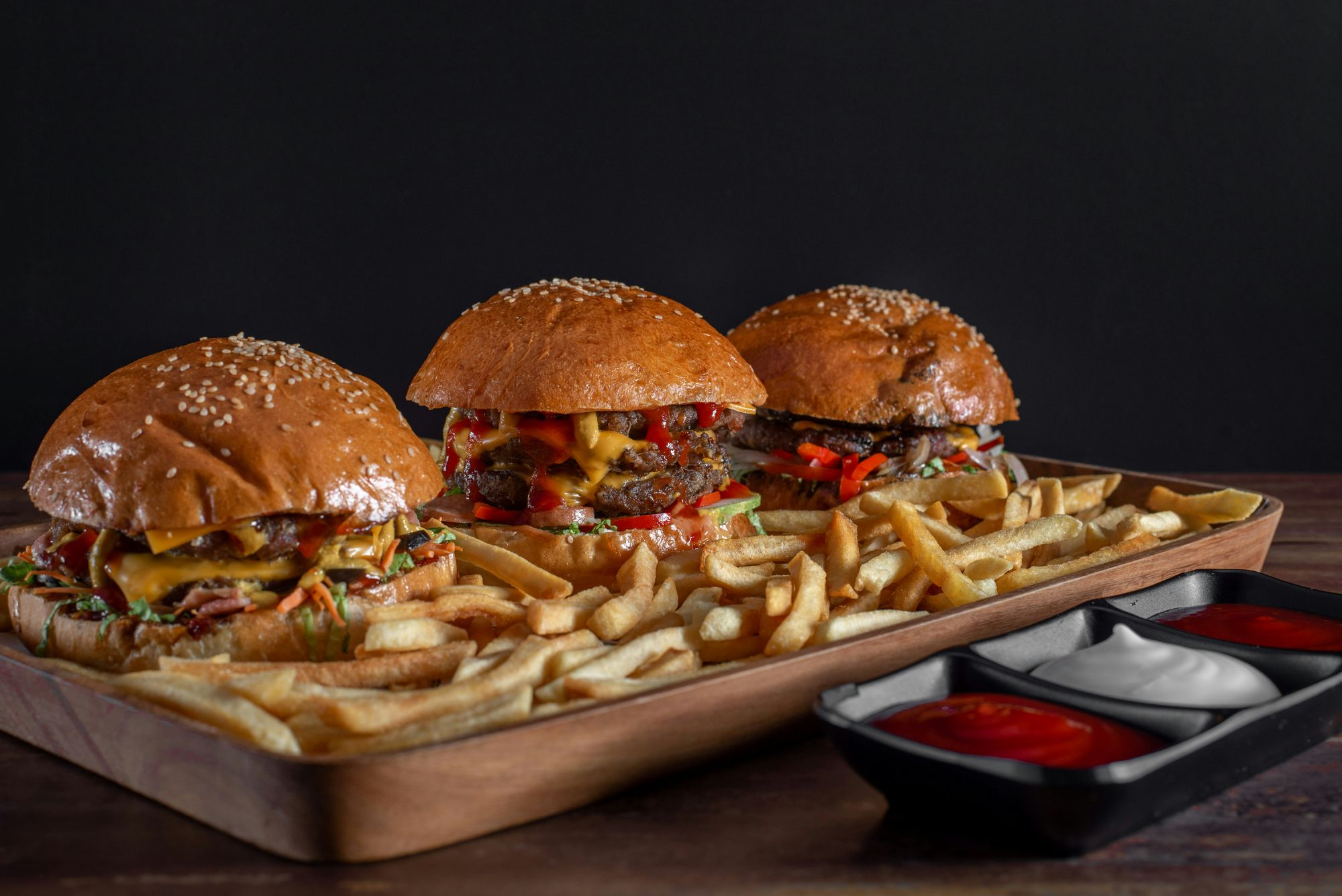 Stół z burgerami, frytkami i sosami, na ciemnym tle, idealne dla miłośników fast food.