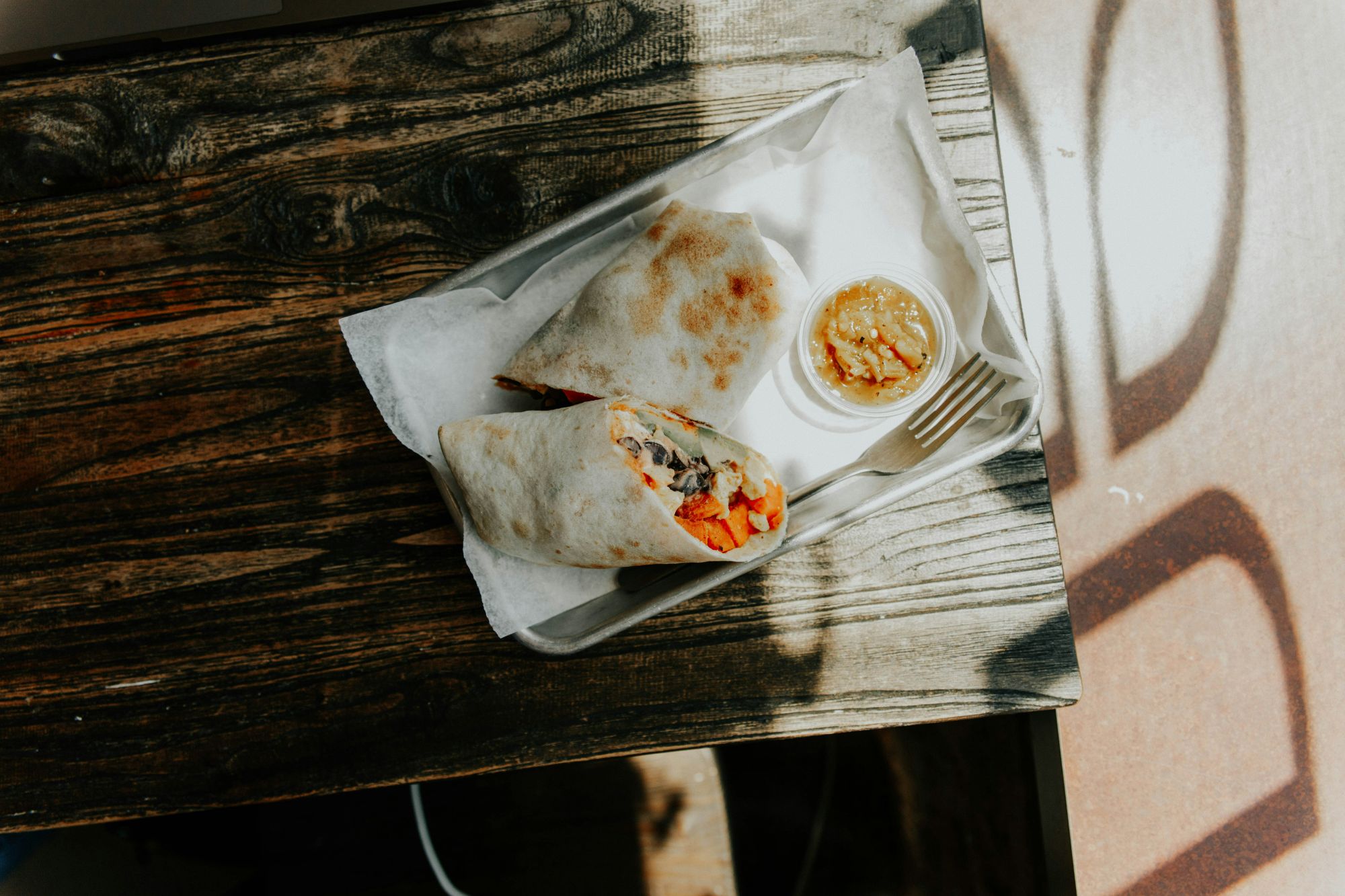 Talerz z burrito i sosem na drewnianym stole, oświetlony naturalnym światłem.