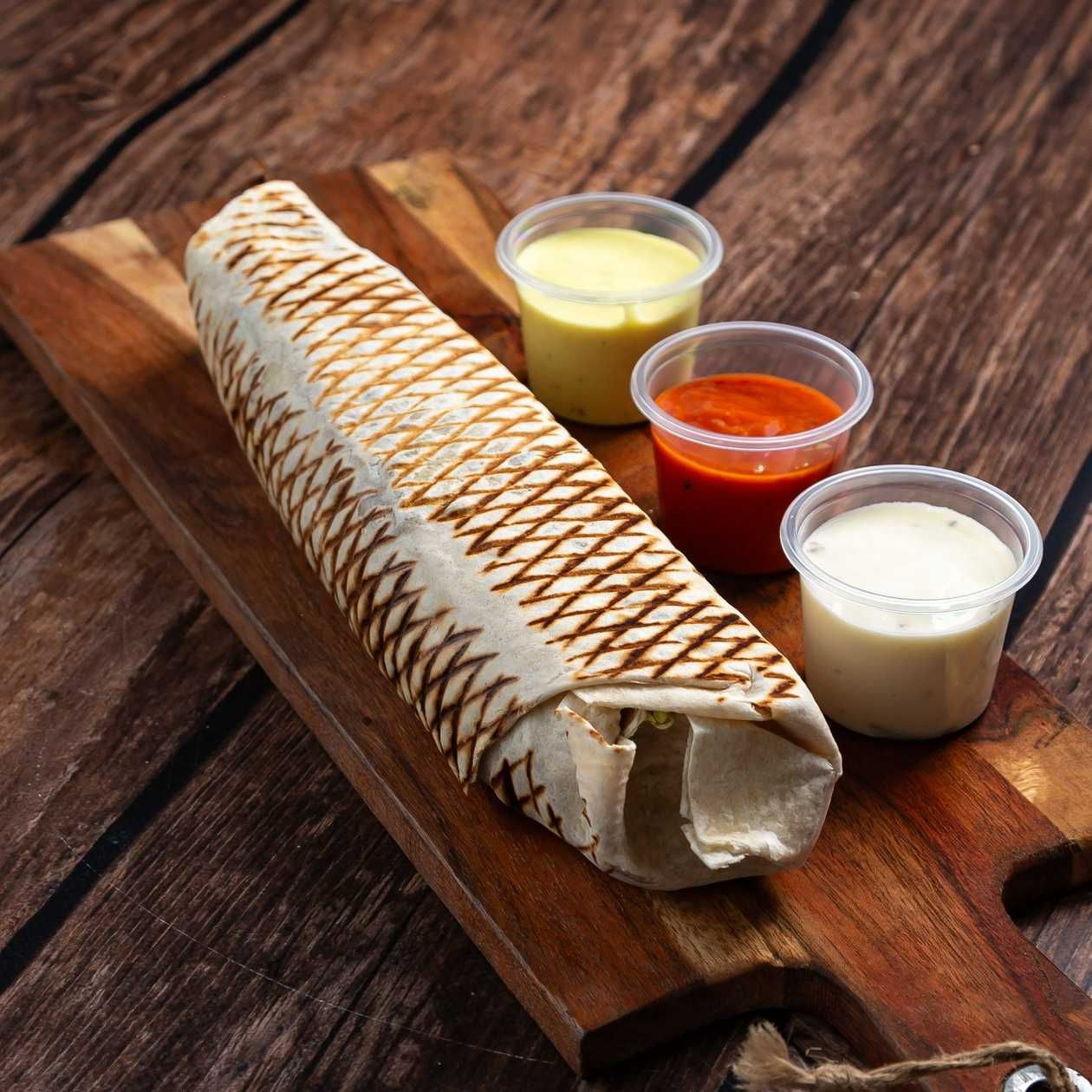Tortilla zapiekana z nadzieniem, podana z trzema sosami w pojemnikach, na drewnianej desce.