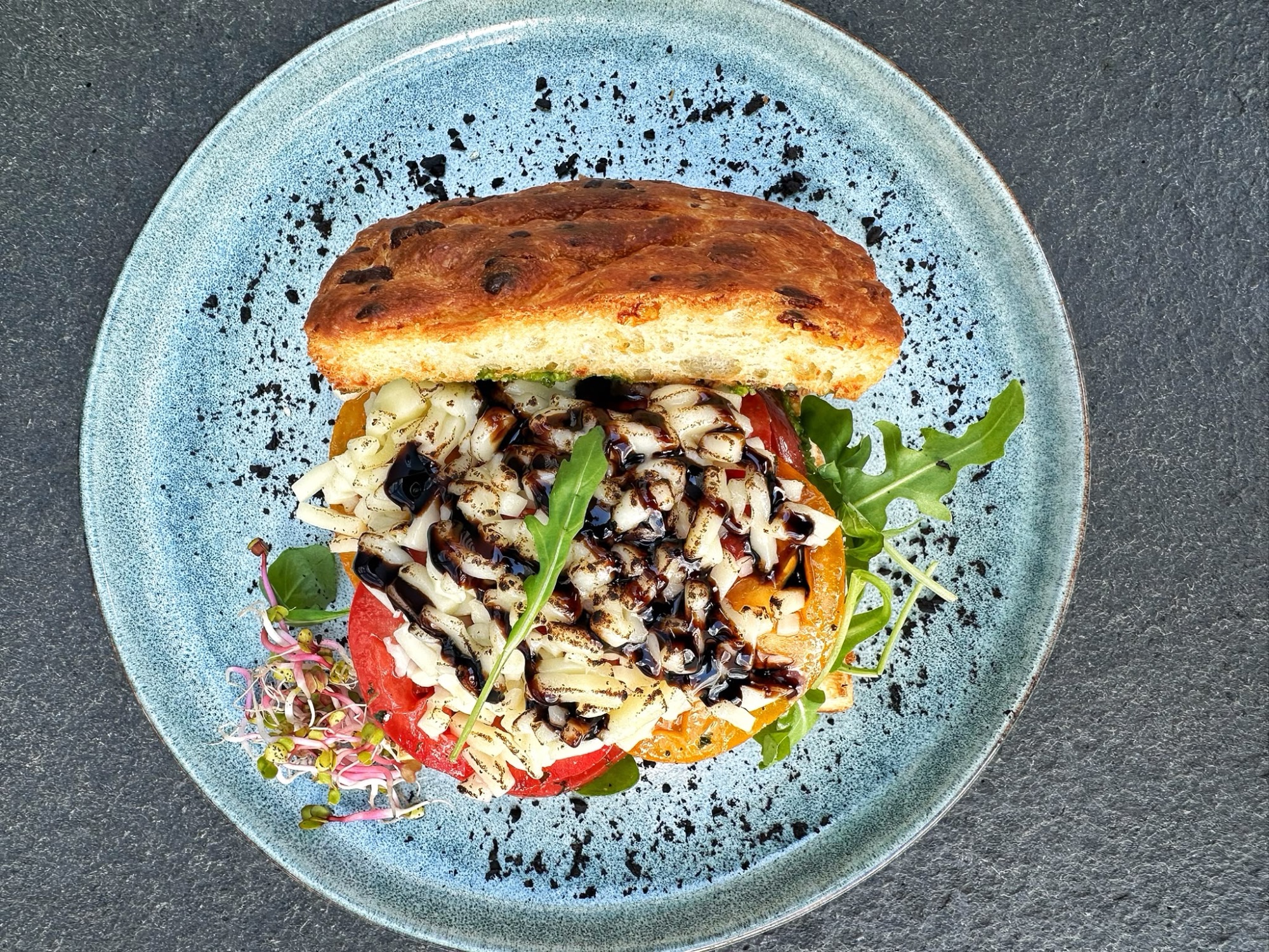 Sandwich z grillowanymi warzywami, serem i rukolą na niebieskim talerzu.